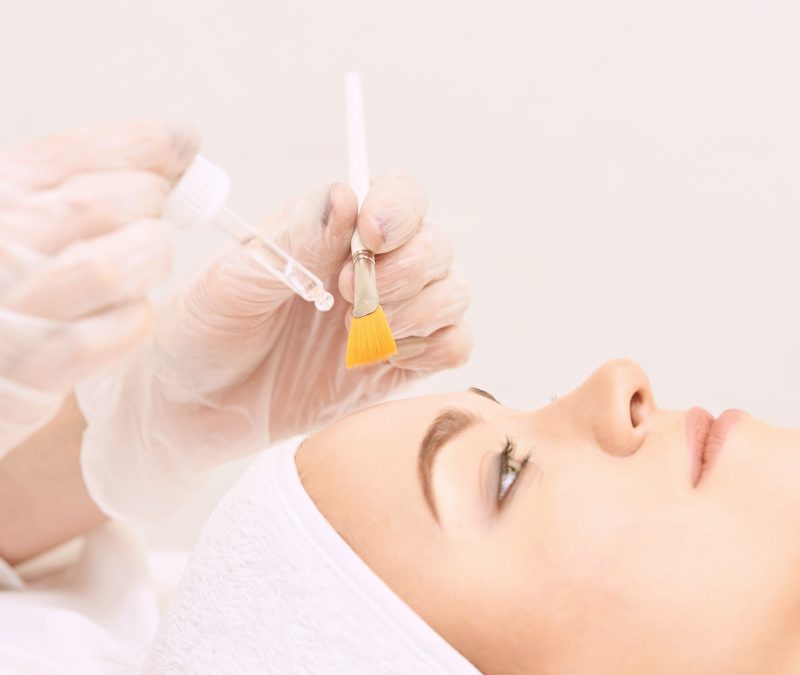 Young woman cleaning face skin in salon. Retinol peel with brush. Acid organic peeling Young woman cleaning face skin in salon. Retinol peel with brush. Acid organic peeling.